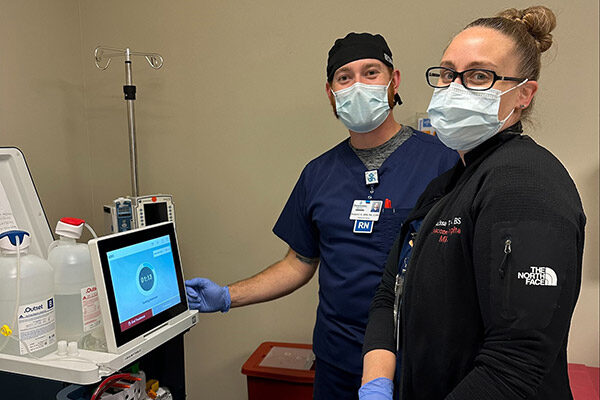 Two nurses standing bedside performing dialysis on a patient with the Tablo Hemodialysis System.