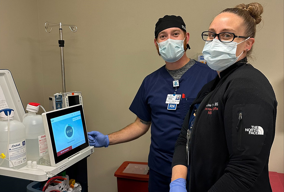 Two nurses standing bedside performing dialysis on a patient with the Tablo Hemodialysis System.