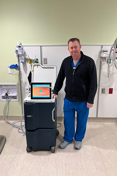 Mike Rauch, MBA, RN, NE-BC, proudly stands next to a Tablo system at Baptist Health Care