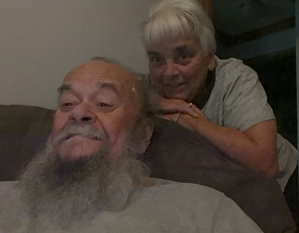 terry-and-marlene Man sitting in a chair with his wife behind him.