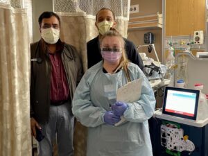Three healthcare professionals standing next to a Tablo Hemodialysis System in a hospital patient room.