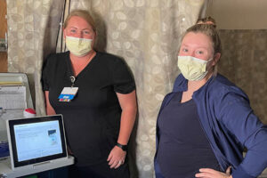 Two female healthcare professionals standing next to a Tablo Hemodialysis System in a hospital patient room